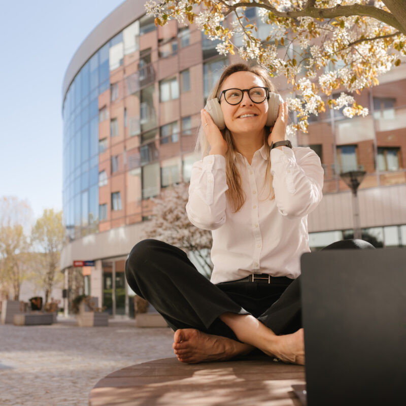 Professional woman working remotely outdoors using technology with headphone on