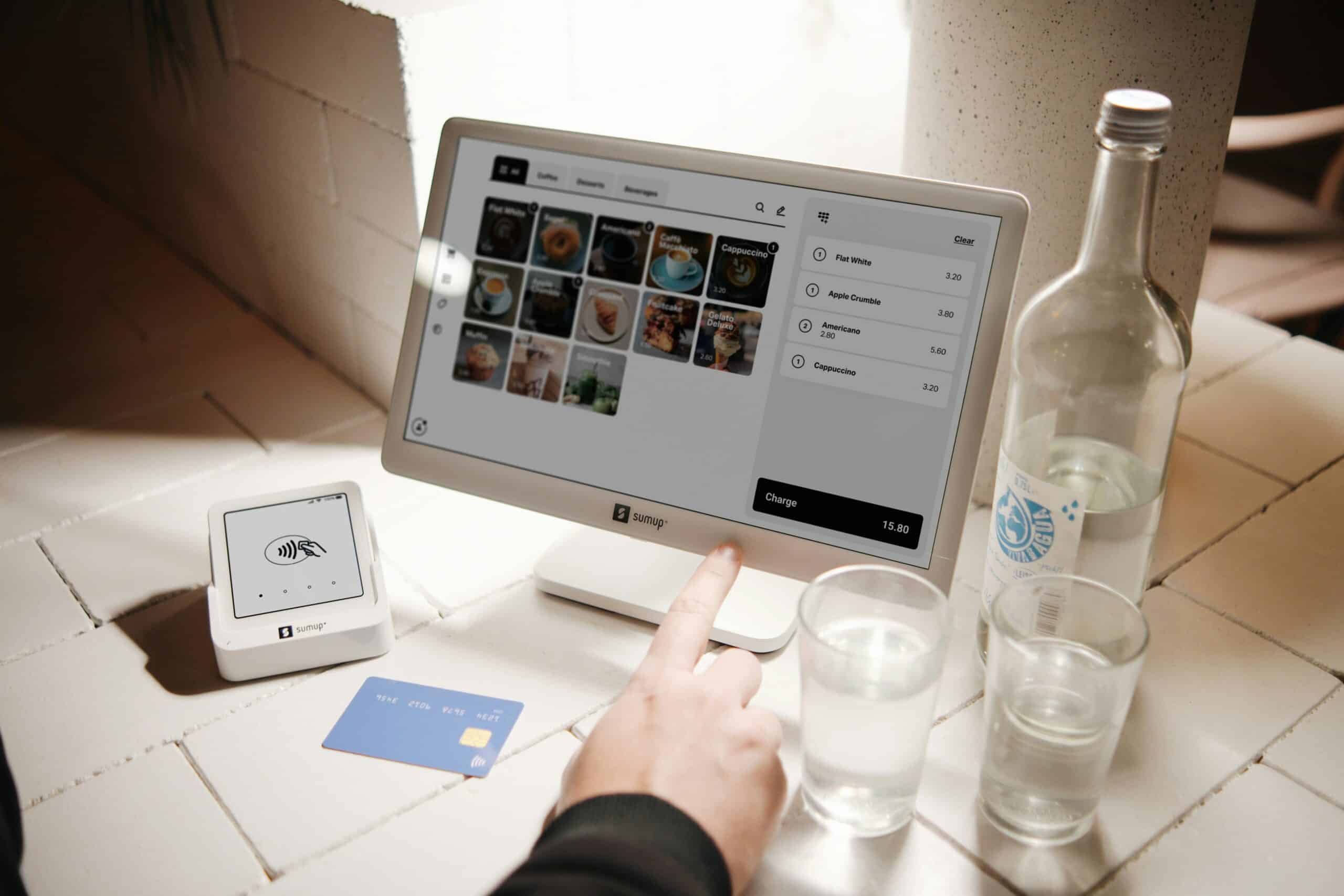 Tablet used for digital payment on a countertop with a credit card and glasses of water