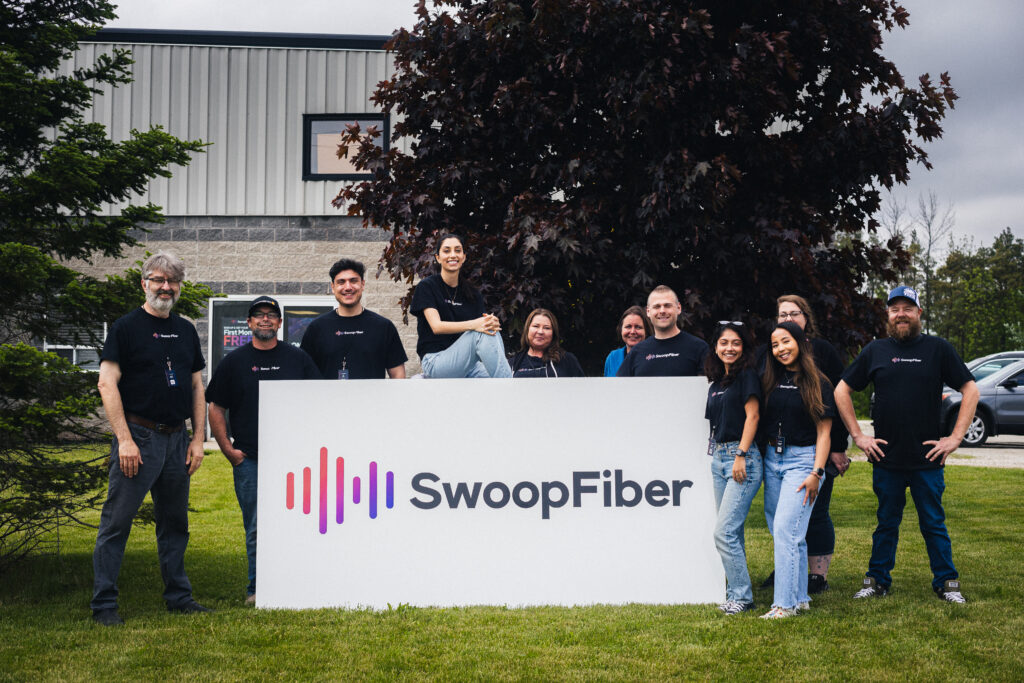 The SwoopFiber team holding a storefront sign on the lawn outside the store.