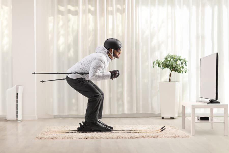 Profile shot of a man skiing at home in a living room in front of tv