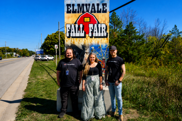 ChatGPT Image May 14, 2026, 07_59_18 PM SwoopFiber team memebers standing outside in front of Elmvale fall fair poster on the side of the road