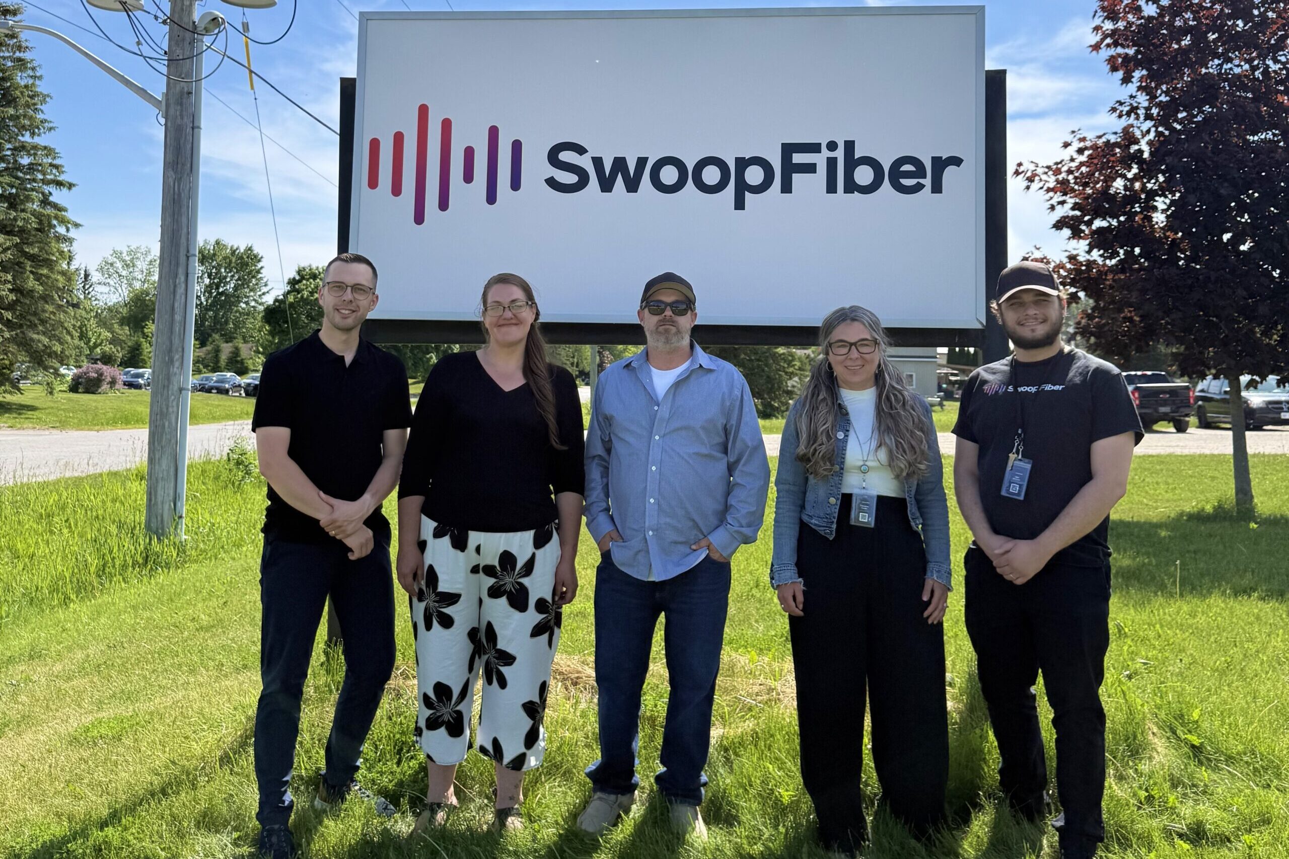 Matt Garwood and the SwoopFiber storefront team pose for a photo in front of the Elmvale storefront sign